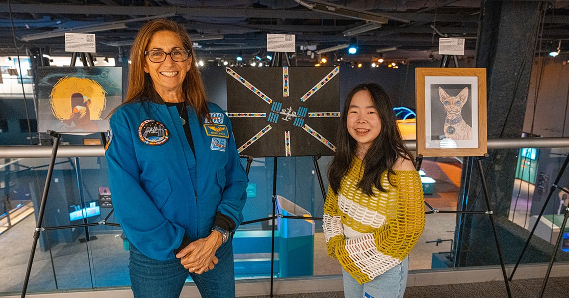 Astronaut, Nicole Stott, stands with a Florida Virtual School student at the FLVS Foundation's Artful Expressions art exhibit, in
